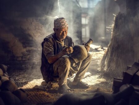 The old man is painting in a clay pot in Durbar square near old hindu temples.